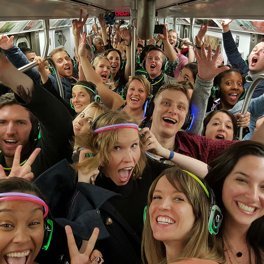Quiet Events Silent Disco headphones for all ages. A group of people on a subway car having fun listening with headphones.