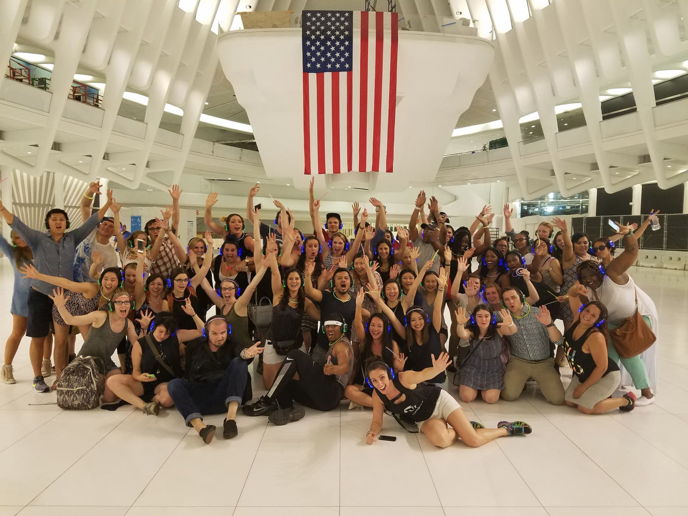 Quiet Events Silent Disco headphones for bar crawls. A large group of people together posing with their hands up in a large space wearing headphones.