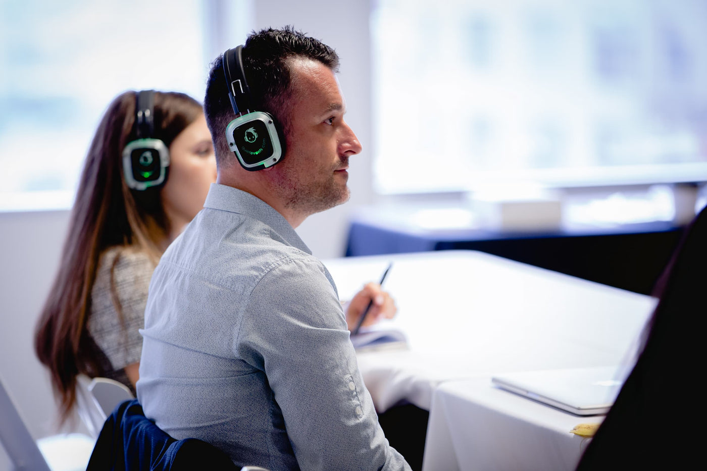 Quiet Events Silent Disco headphones for conferences two people with headphones sitting behind a table paying attention.