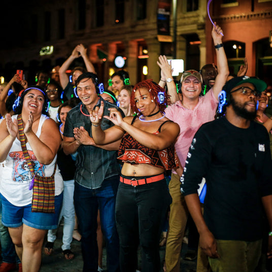 Quiet Events Silent Disco headphones for dance parties a group of people cheering and having fun while listening to music with headphones.