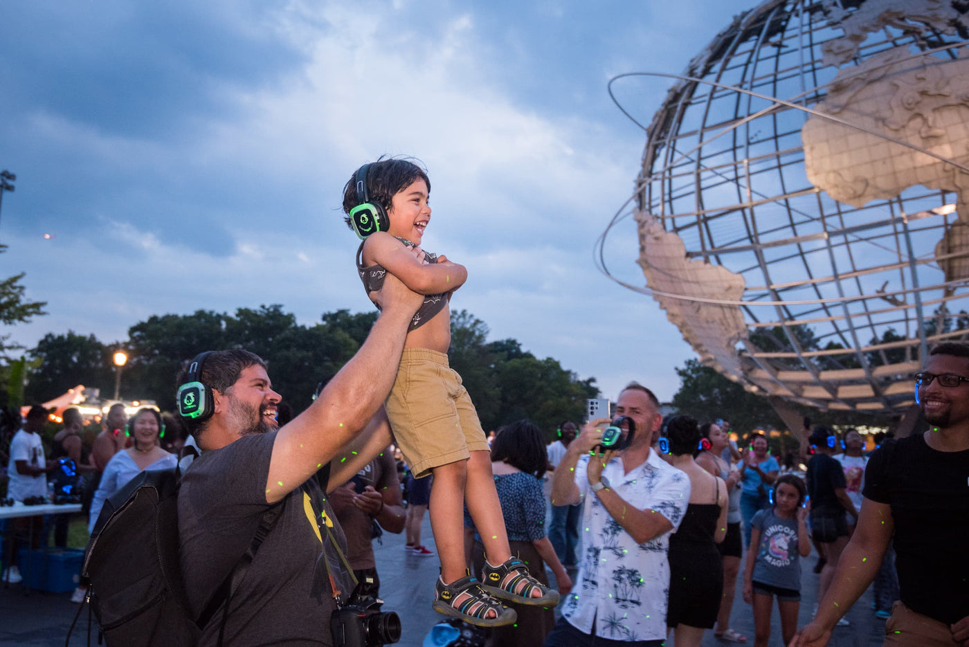 Quiet Events Silent Disco headphones for kids. A Dad lifts his son in front of him up in the air at the park.
