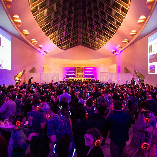 Quiet Events Silent Disco headphones for dance parties a group of people dancing on having fun inside a large open space inside building.