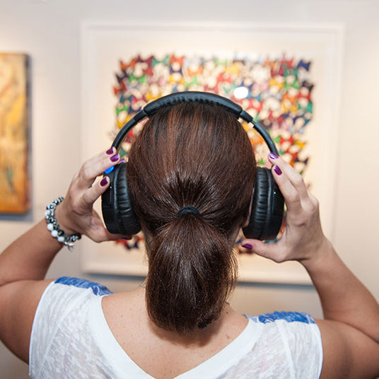 Quiet Events Silent Disco headphones for dance parties a woman at a museum wearing headphones and reaching to adjust them.