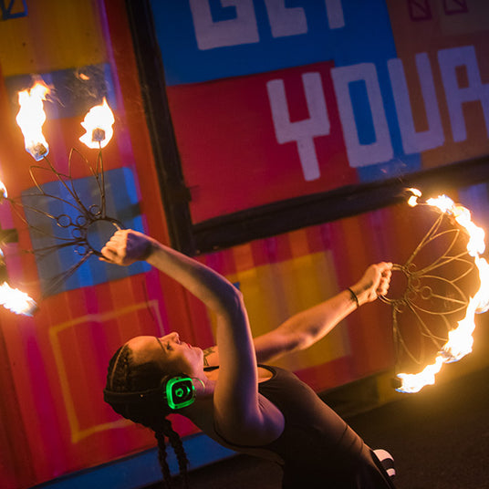 Quiet Events Silent Disco headphones for fairs a woman juggling fire sticks at night wearing headphones