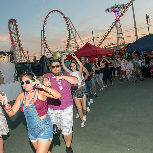 Quiet Events Silent Disco headphones for state fairs a group of people dancing one behind another in a single line at an amusement park