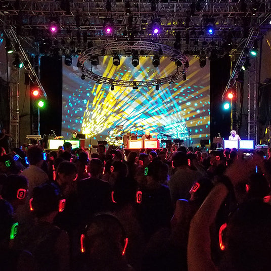 Quiet Events Silent Disco headphones for fairs a group of people wearing headphones dancing to the dj's on stage.