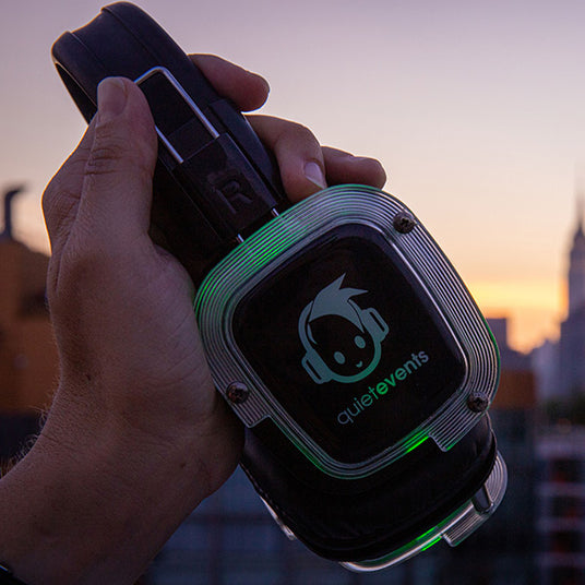 Quiet Events Silent Disco headphones for fairs with an upclose side view of headphones glowing in green color held in a hand