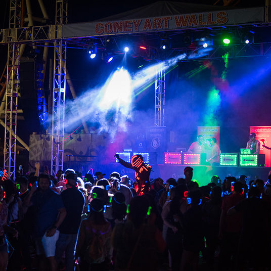 Quiet Events Silent Disco headphones for a festival at night outdoors a group of people dancing and with a stage on with three DJ's