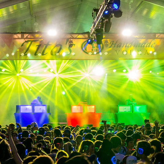 Quiet Events Silent Disco headphones for festivals a group of people gather together with headphones listening to three dj's on a stage.