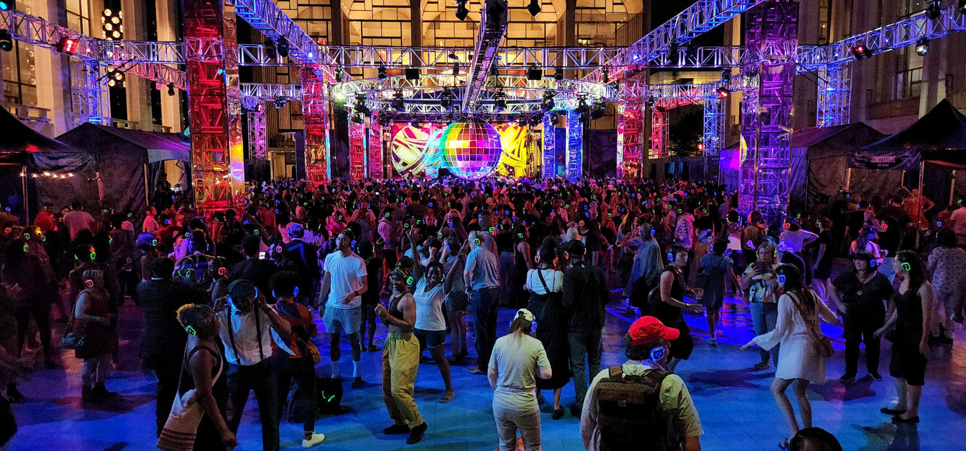 Quiet Events Silent Disco headphones for festivals a group of people dancing outdoors having fun.