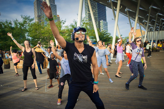 Quiet Events Silent Disco headphones for fitness. An Instructor giving an aerobic class to others outdoors having fun wearing headphones.