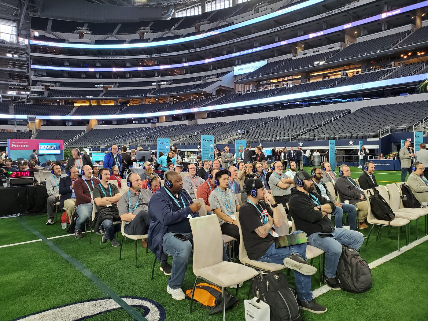 Quiet Events Silent Disco headphones for convention a group of people sitting wearing headphones paying attention to a speaker inside a football stadium field.