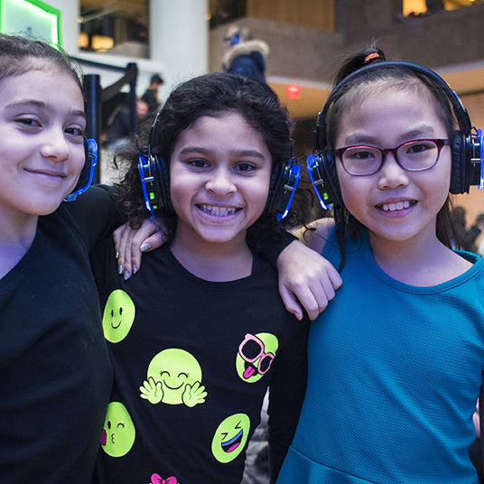 Quiet Events Silent Disco headphones for home and a group of three young female children with headphones embracing eachother.