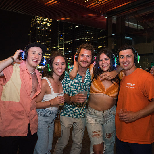 Quiet Events Silent Disco headphones for hotels. A group of four people gather together at a party having fun and wearing headphones.