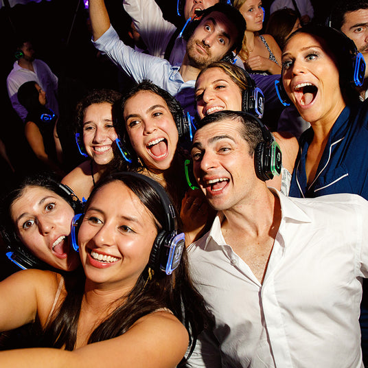 Quiet Events Silent Disco headphones for hotels. A group of people gather together smiling and posing for a picture with headphones.