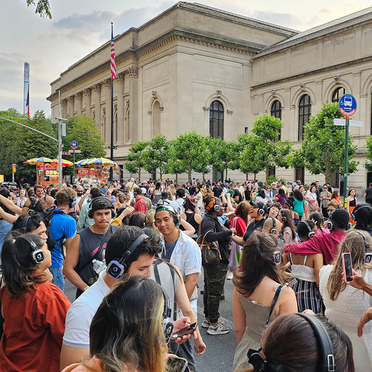 Quiet Events Silent Disco headphones for museums. A group of people standing outside a museum during the day wearing headphones.
