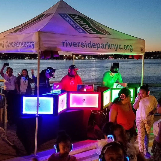 Quiet Events Silent Disco headphones for parks. A group of DJ's underneath a tent outdoors playing music for others.