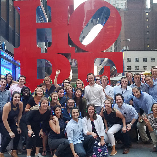 Quiet Events Silent Disco headphones for schools. A group of people gather together outdoors posing for a picture with headphones.