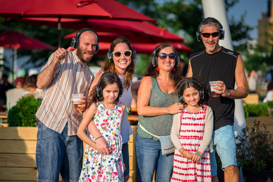 Quiet Events Silent Disco headphones for traveling. A group of people adults and children outdoors having fun with headphones.