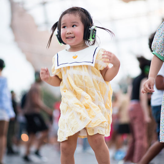 Quiet Events Silent Disco headphones for kids.  A baby asian little girl having fun at the park with headphones.