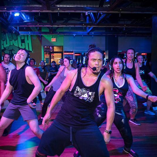 Quiet Events Silent Disco headphones for fitness and meditation.  A gym instructor with a full dance class wearing headphones.