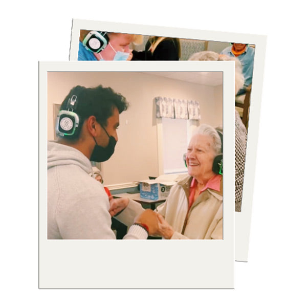 Quiet Events Silent Disco headphones for senior care.  An older woman been helped by someone having fun holding hands and wearing headphones.